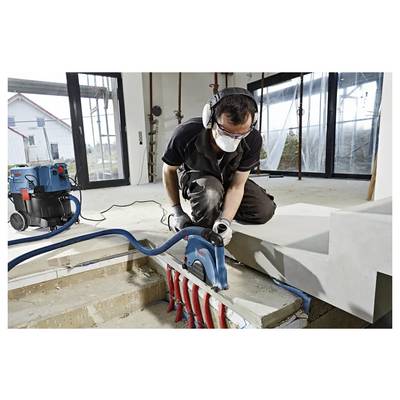 Ein Arbeiter nutzt ein Elektrowerkzeug, um Beton in einem teilweise konstruierten Gebäude zu schneiden, trägt Schutzausrüstung und kniet neben Treppen.