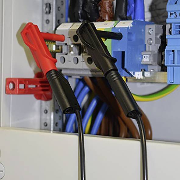 Ein elektrisches Schaltschrank-Innenleben mit roten und schwarzen Prüfspitzen, die an einem Kabel angeschlossen sind.
