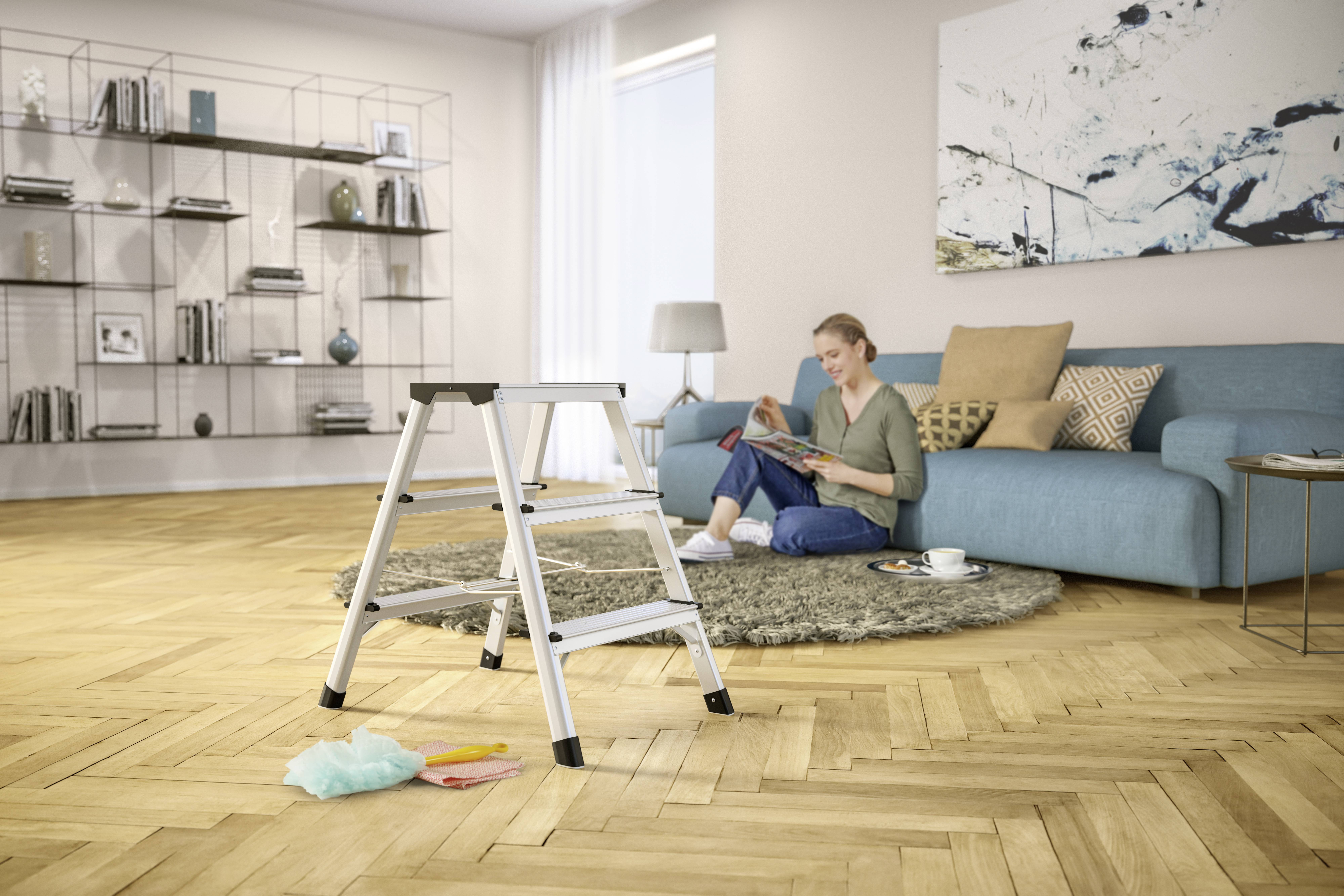 Eine Person sitzt auf einem blauen Sofa in einem Wohnzimmer, liest ein Buch. Im Vordergrund steht eine kleine Leiter.