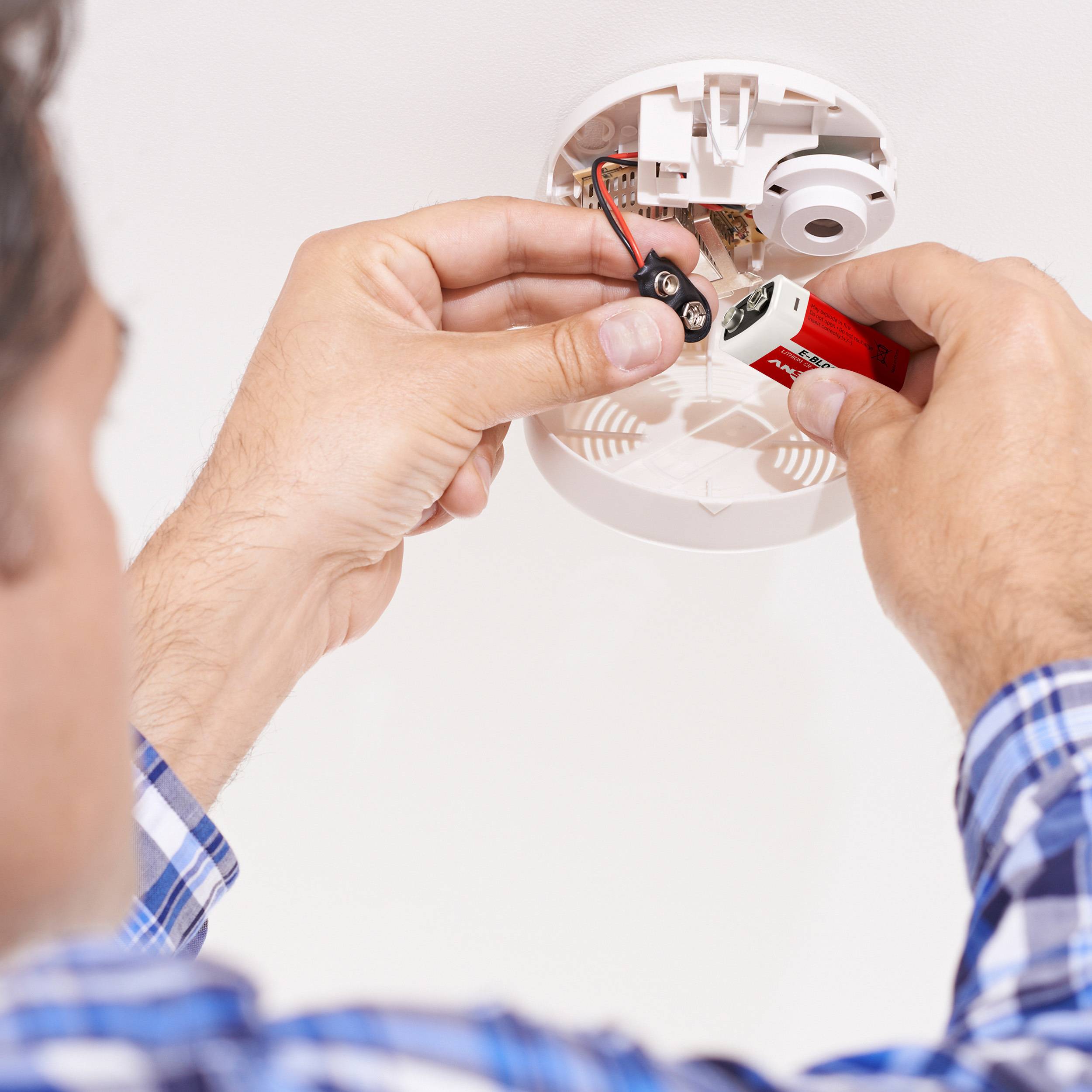 Eine Person installiert einen Rauchmelder an einer Decke und verbindet die Kabel mit einer Batterie.