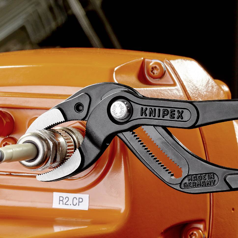 'KNIPEX Cobra'-Zange hält einen Metalladapter an einer orangefarbenen Maschine mit Aufkleber 'R2.CP'.