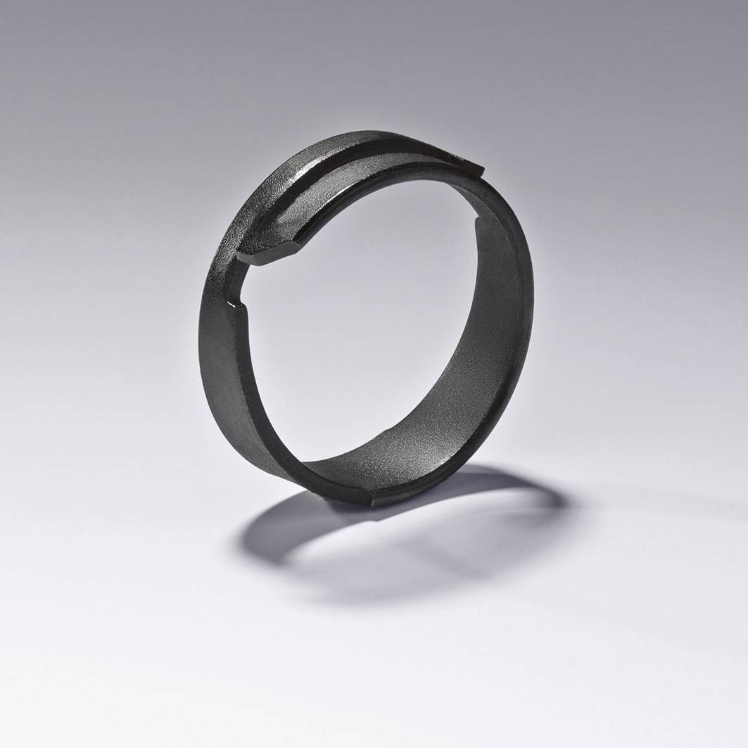 Ein schwarzer, runder Metallring mit einer Einkerbung liegt auf einer glatten Oberfläche und wirft einen Schatten.