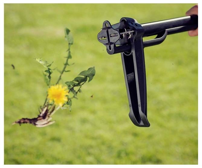 Ein Werkzeug entfernt eine Löwenzahnpflanze, einschließlich Wurzeln und Erde, aus einem Rasenstück und demonstriert seine Funktion bei der Unkrautbeseitigung.