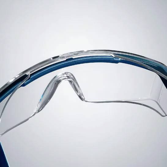 Schutzbrille in Nahaufnahme mit transparenten Gläsern und blauen Bügeln, vor hellem Hintergrund.