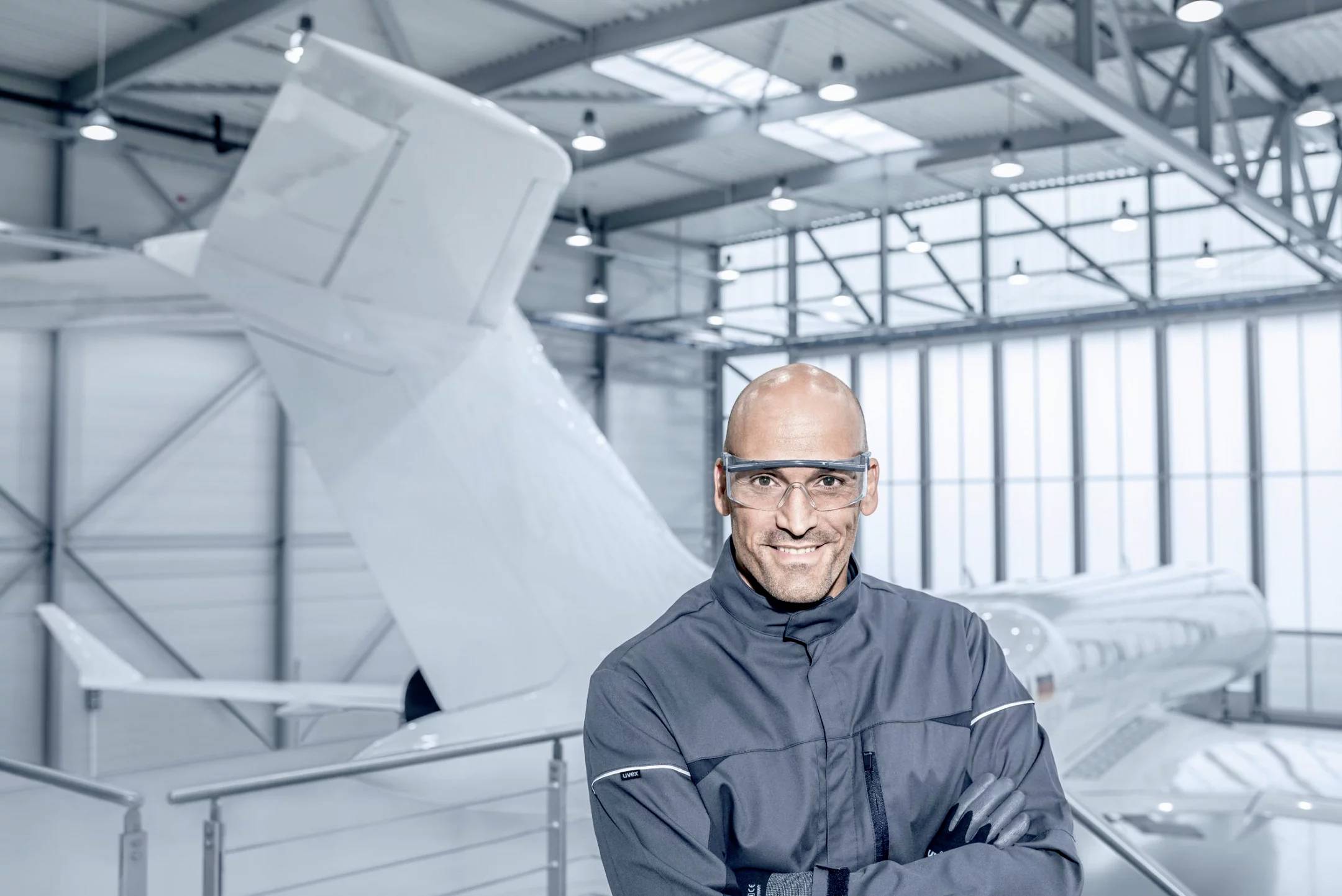 Ein Mann mit Schutzbrille steht lächelnd in einem Hangar vor einem Flugzeug.