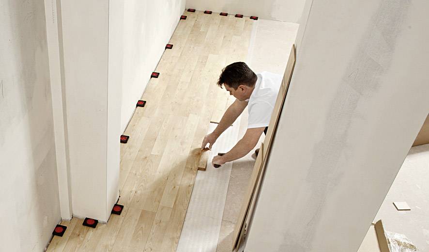 Ein Mann verlegt Laminatboden in einem Flur. Er kniet auf dem Boden und passt die Bretter präzise an, um den Raum gleichmäßig zu bedecken.
