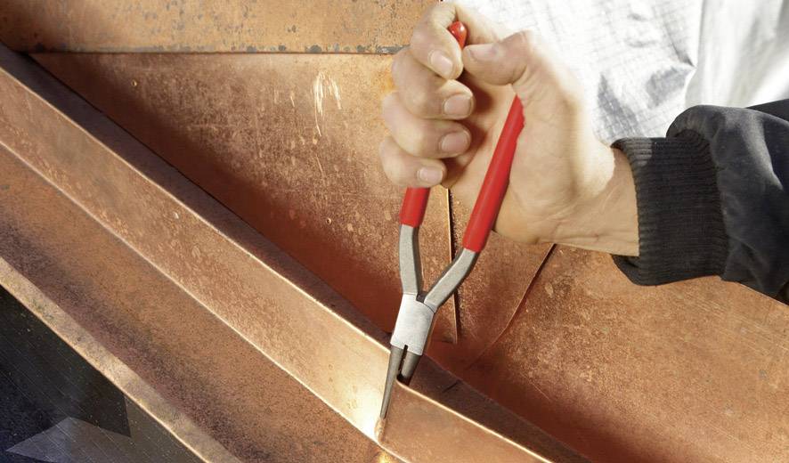 Hand, die mit einer roten Zange ein Kupferblech bearbeitet.