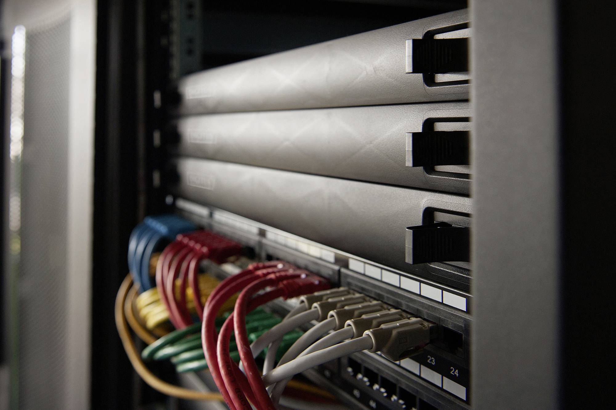 Server-Rack mit mehreren Netzwerk-Kabeln in verschiedenen Farben, die an der Rückseite angeschlossen sind.