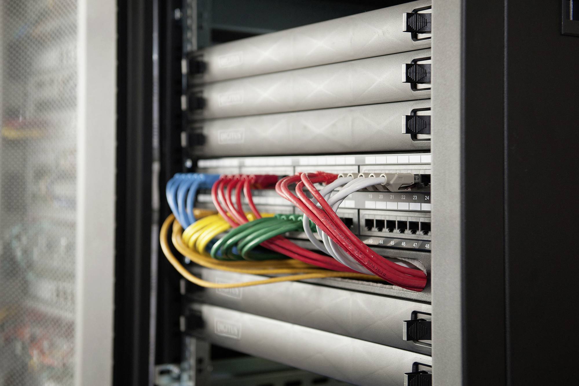 Ein Serverschrank mit mehreren Netzwerkroutern und farbigen Kabeln, die in Portleisten eingesteckt sind.
