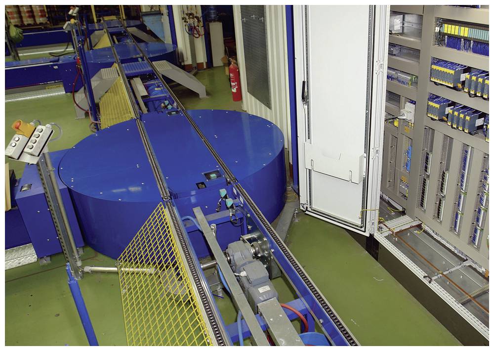 Maschine in einer Fabrikumgebung mit blauen und gelben Elementen, Förderband, Steuerkonsole und elektrischen Schaltschränken.