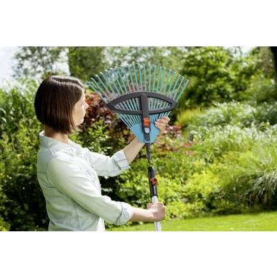 Person hält einen verstellbaren Rechen im Garten. Umgeben von grünem Laub und Pflanzen. Sie überprüft die Werkzeugeinstellung.