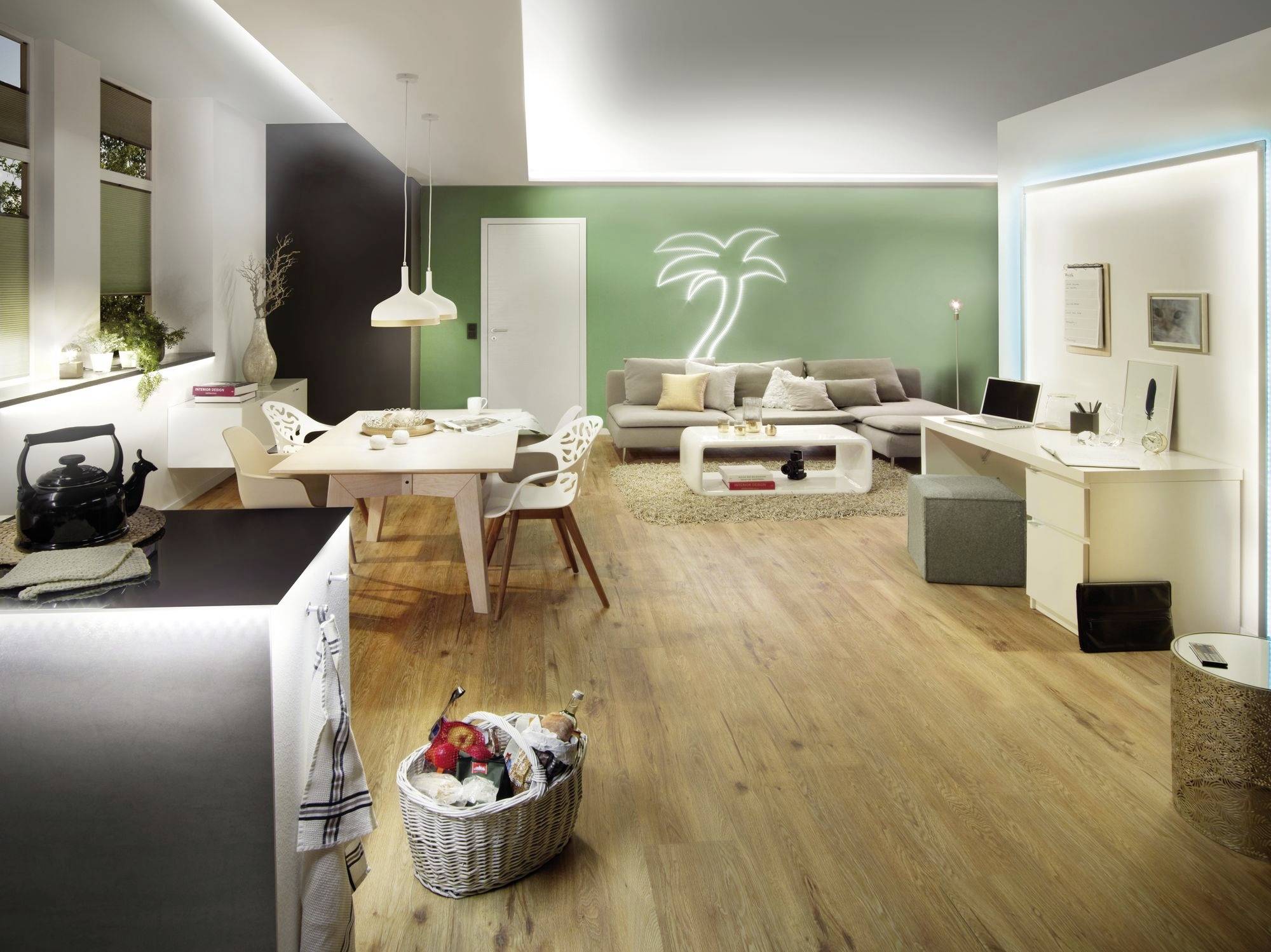 Ein modernes Wohnzimmer mit Holzboden, grüner Wand mit Leuchtreklame einer Palme, Essbereich links und Schreibtisch rechts.