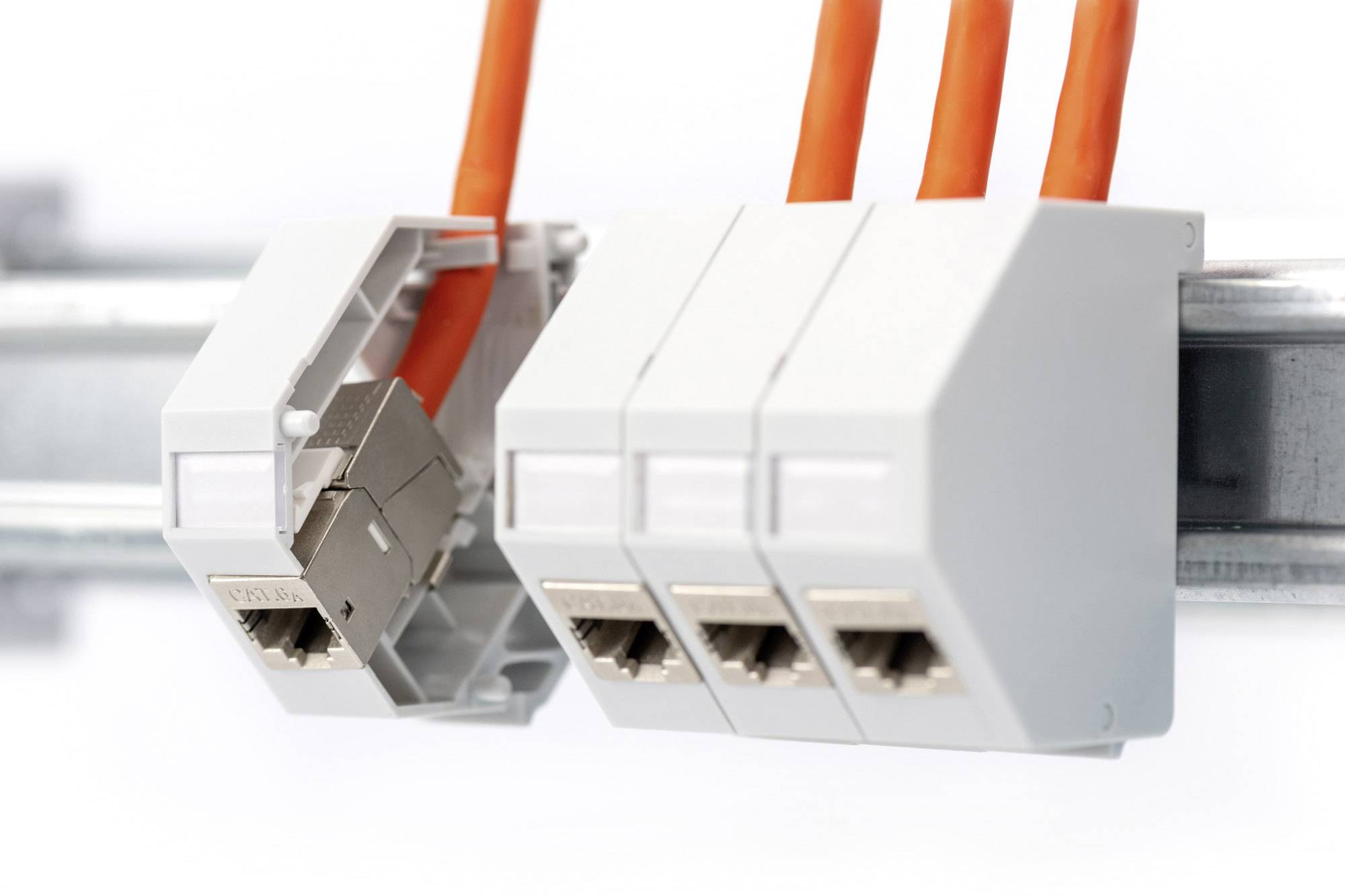 'Drei weiße Klemmen mit orangefarbenen Kabeln auf Montageschiene, zeigen installierte elektrische Verbindungen.'