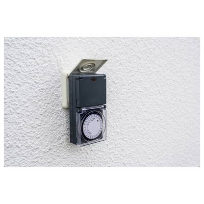 Ein wandmontierter elektrischer Zeitschalter mit Zifferblatt und durchsichtiger Abdeckung auf einer strukturierten weißen Wand.