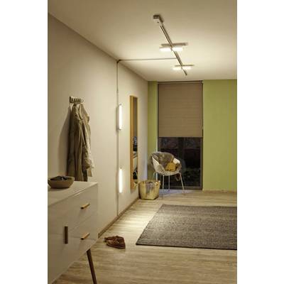 Ein Wohnzimmer mit einer beigen Wand, an der ein Mantel hängt. Ein Stuhl mit Decke, Spiegel, Lampe auf Kommode und ein Teppich auf Holzboden.