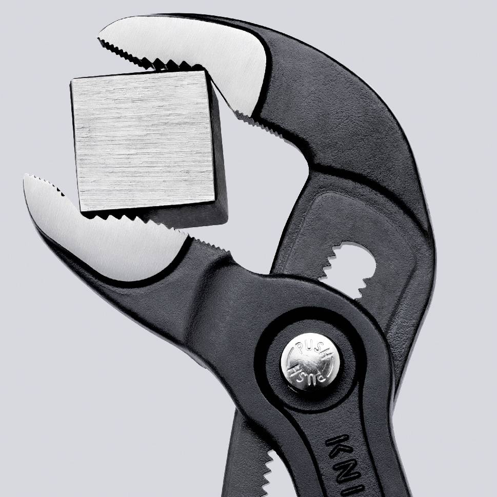 Eine Zange hält einen Metallwürfel fest. Die Zange ist verstellbar und aus schwarzem Metall.