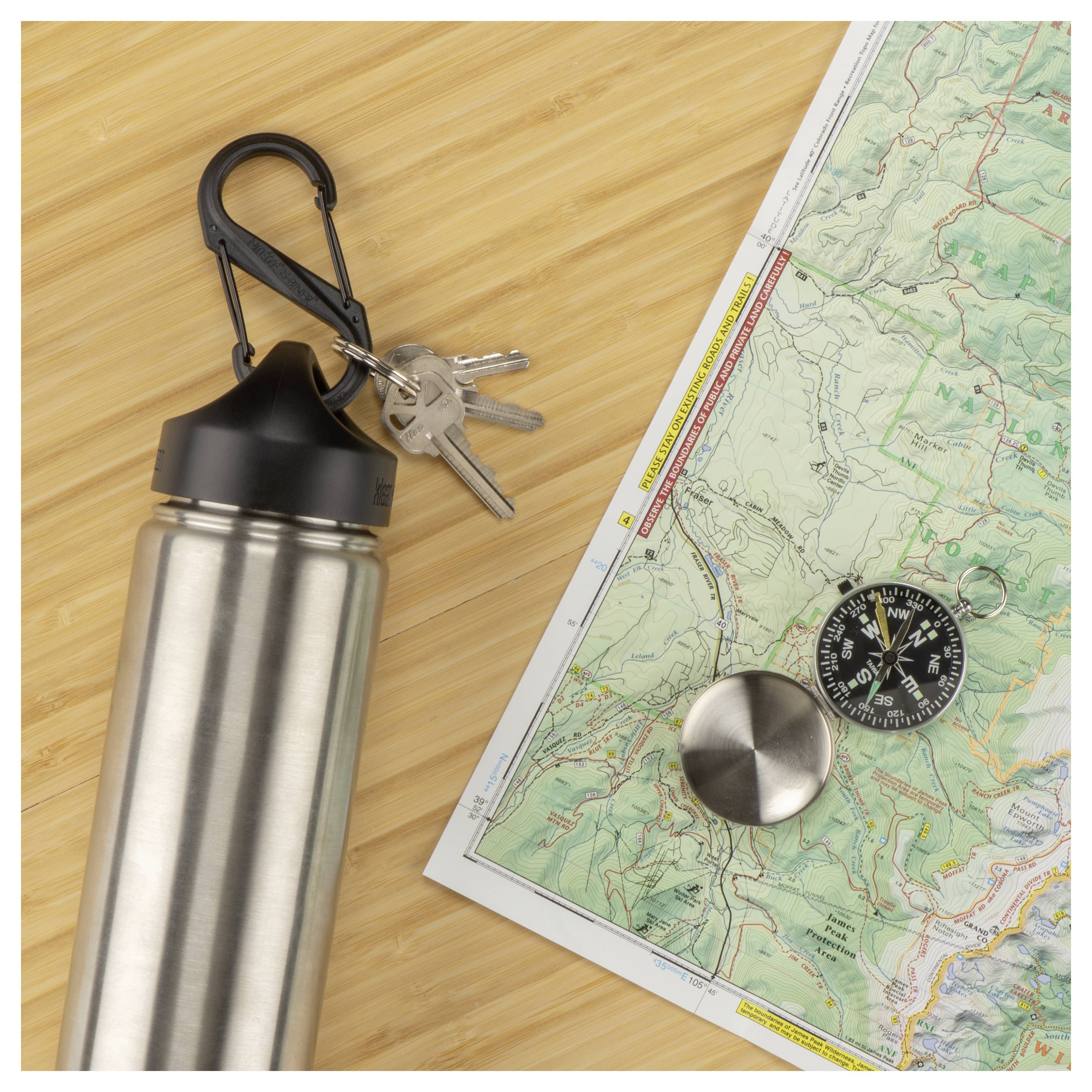 Eine Metallwasserflasche mit Schlüsseln ist neben einem Kompass auf eine Karte geklippt, was Navigation oder Wandervorbereitung andeutet.