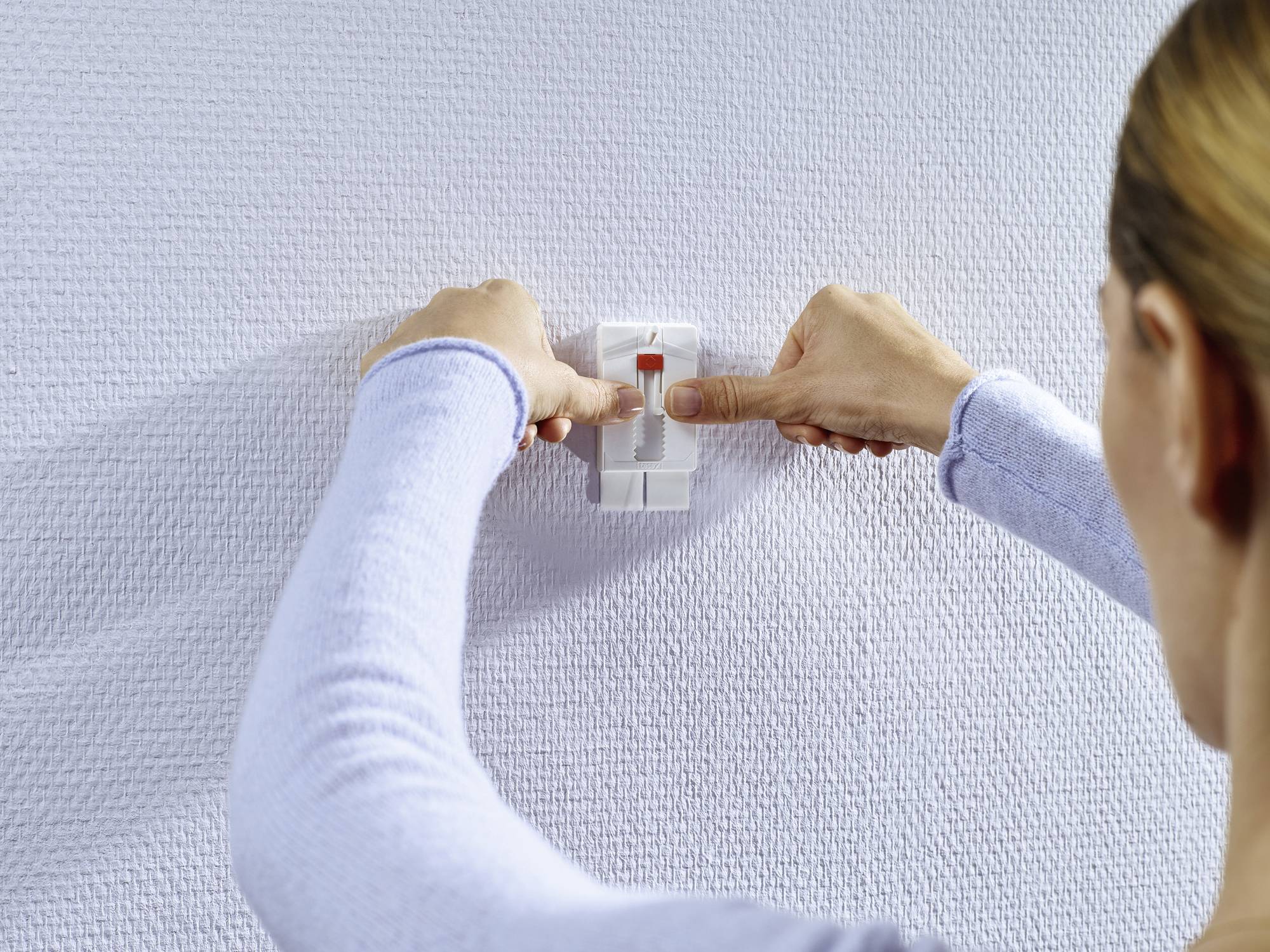 Eine Person befestigt einen Bildaufhängestreifen an einer strukturierten Wand. Der Streifen wird mittig ausgerichtet.