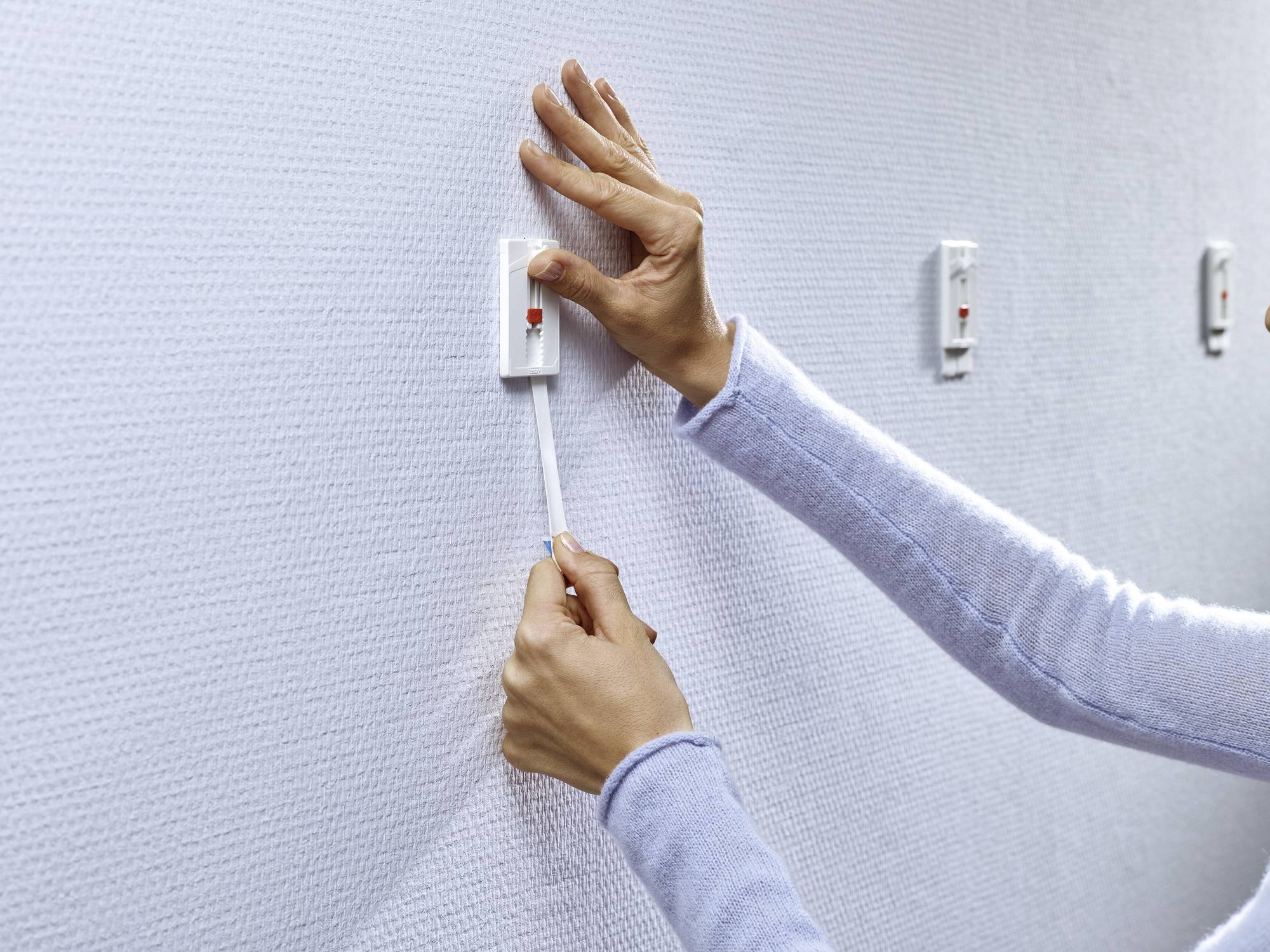 Eine Hand zieht an einem Schnurlichtschalter an einer weißen Wand. Der Schalter ist rechteckig und an einer strukturierten Oberfläche befestigt.