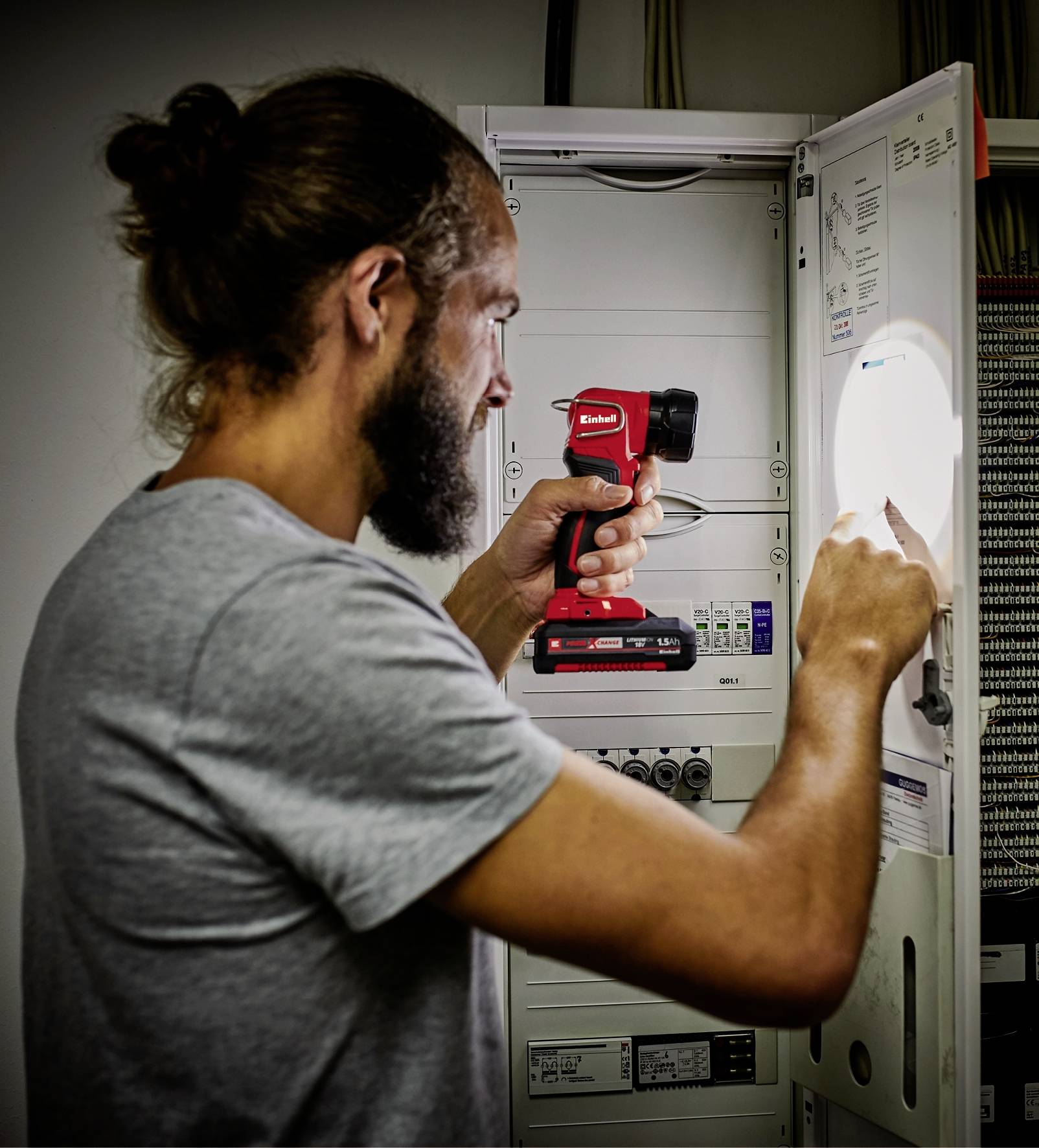 Eine Person repariert einen Schaltschrank mit einem Elektrowerkzeug. Sie trägt ein graues T-Shirt und konzentriert sich auf die Arbeit im Inneren des Schranks.