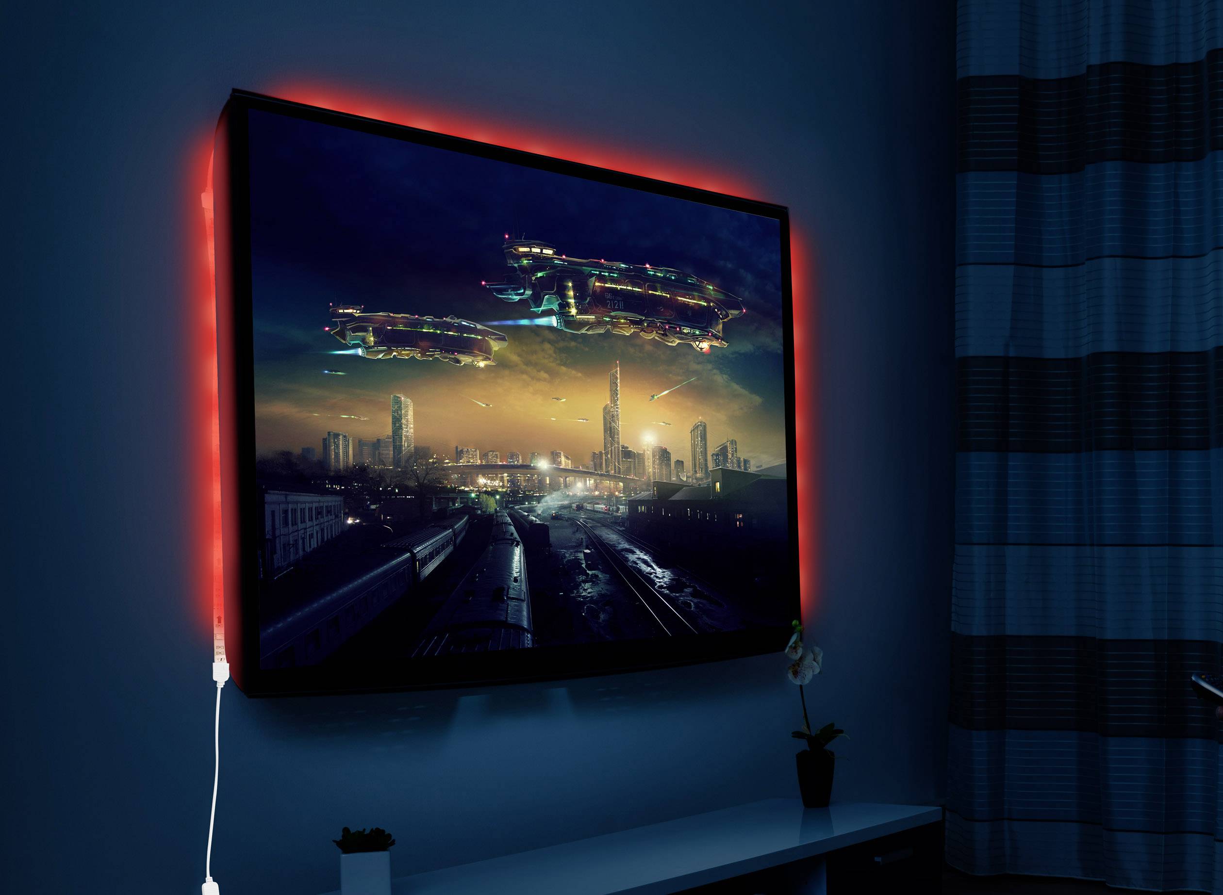 Ein an der Wand montierter Fernseher zeigt ein beleuchtetes Stadtbild bei Nacht. Der Bildschirm ist von rotem Licht umgeben.