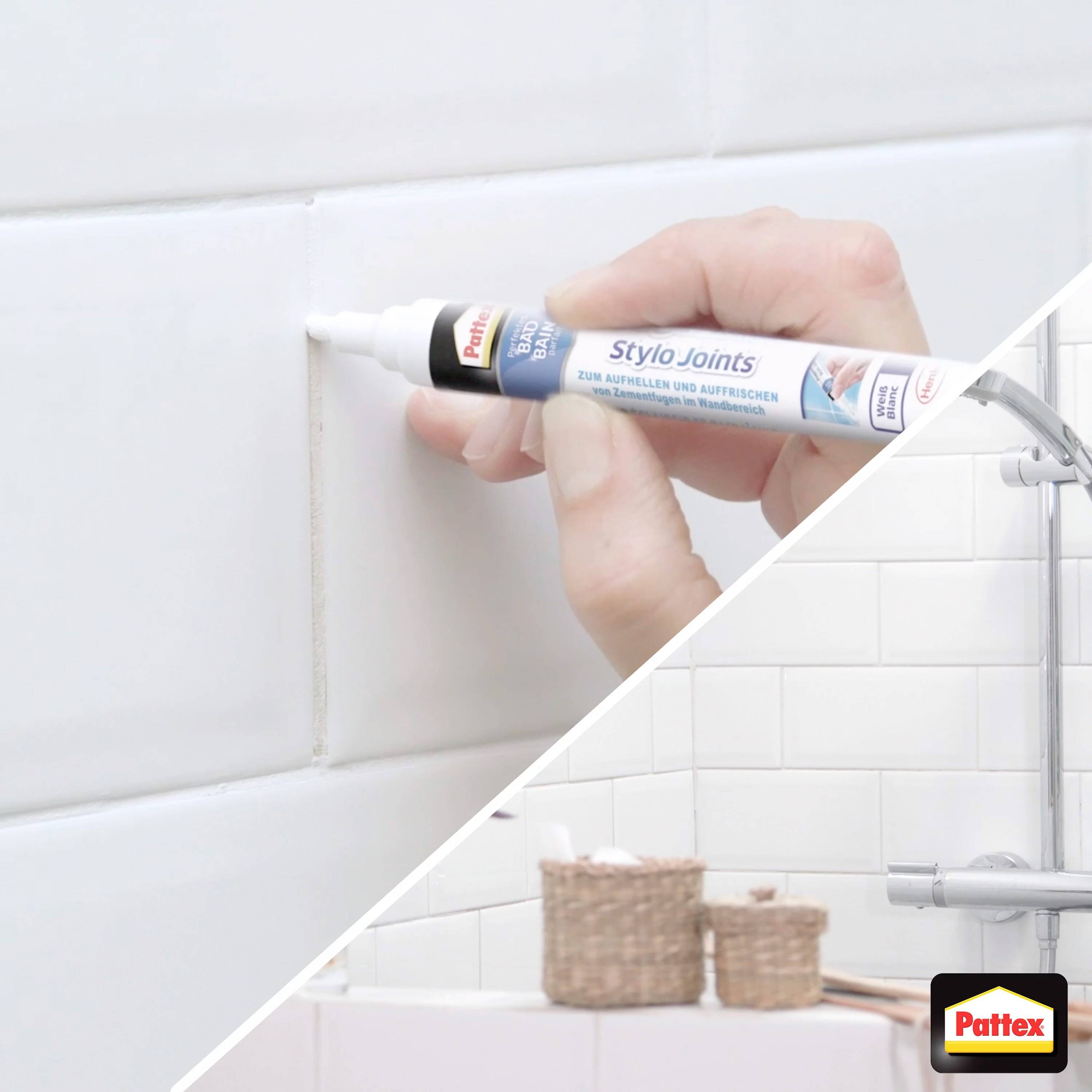 Eine Hand hält einen Stylo Joints-Marker und erneuert Fugen zwischen weißen Badezimmerfliesen. Ein Bad mit gefliesten Wänden im Hintergrund.