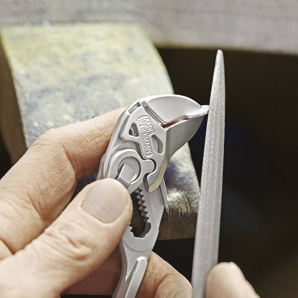 Eine Person benutzt eine Feile und eine Zange, um die Zahnoberfläche der Zange zu bearbeiten. Die Zange ist auf ein Metallstück gestützt.