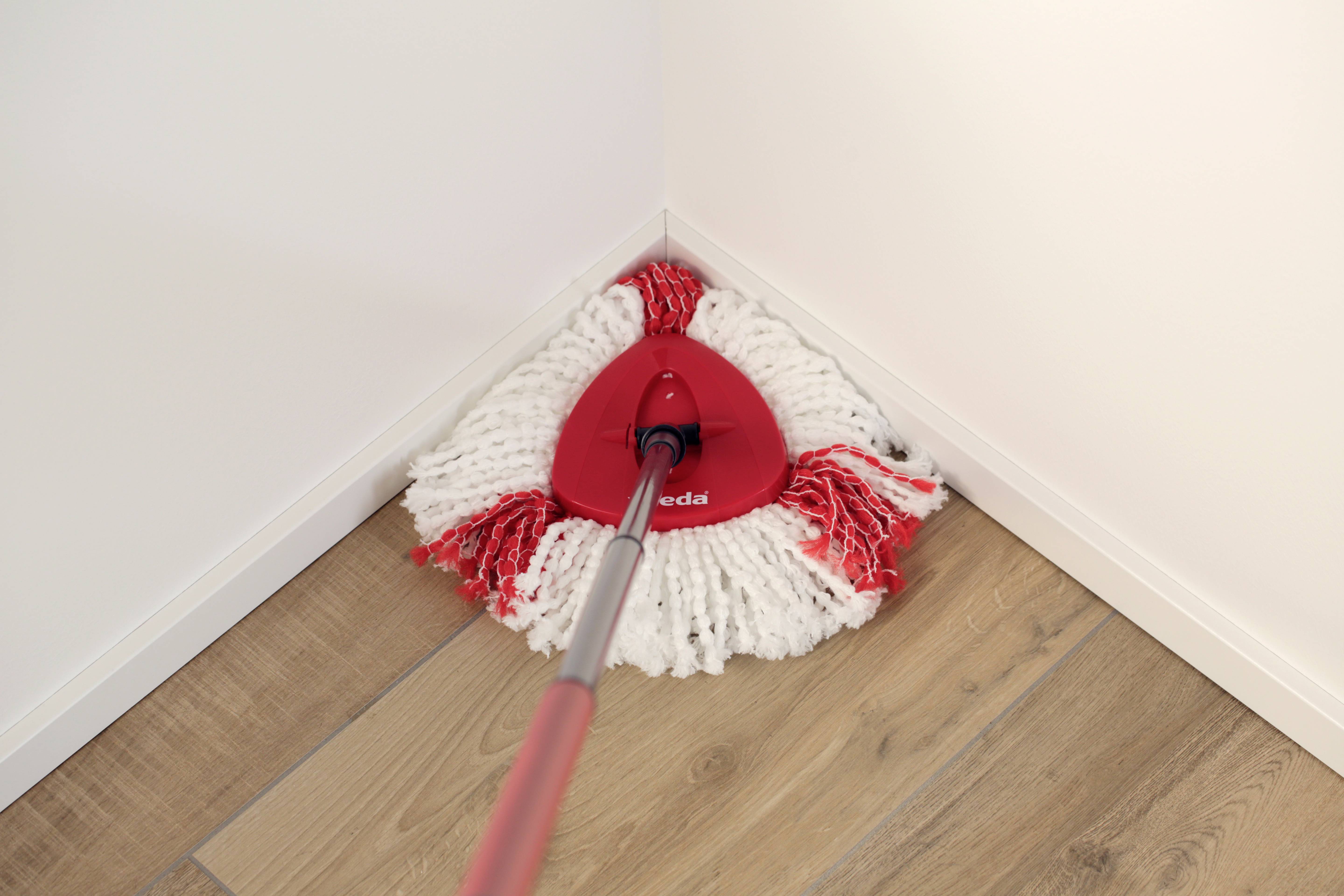 Ein roter Dreiecksmopp mit weißem Mopkopf reinigt eine Ecke auf einem Holzboden.