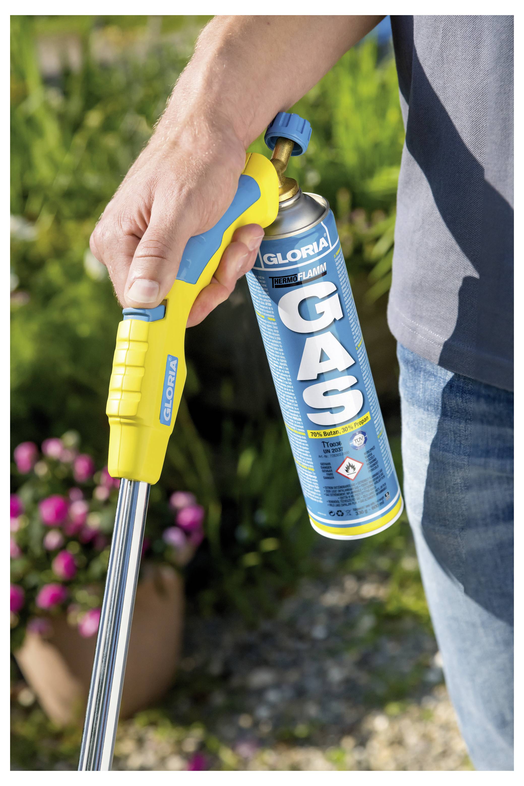 Person, die eine GLORIA GAS-Fackel mit einer gelben Düse und angebrachtem Gaskanister hält, bereit zur Verwendung im Freien im Garten.