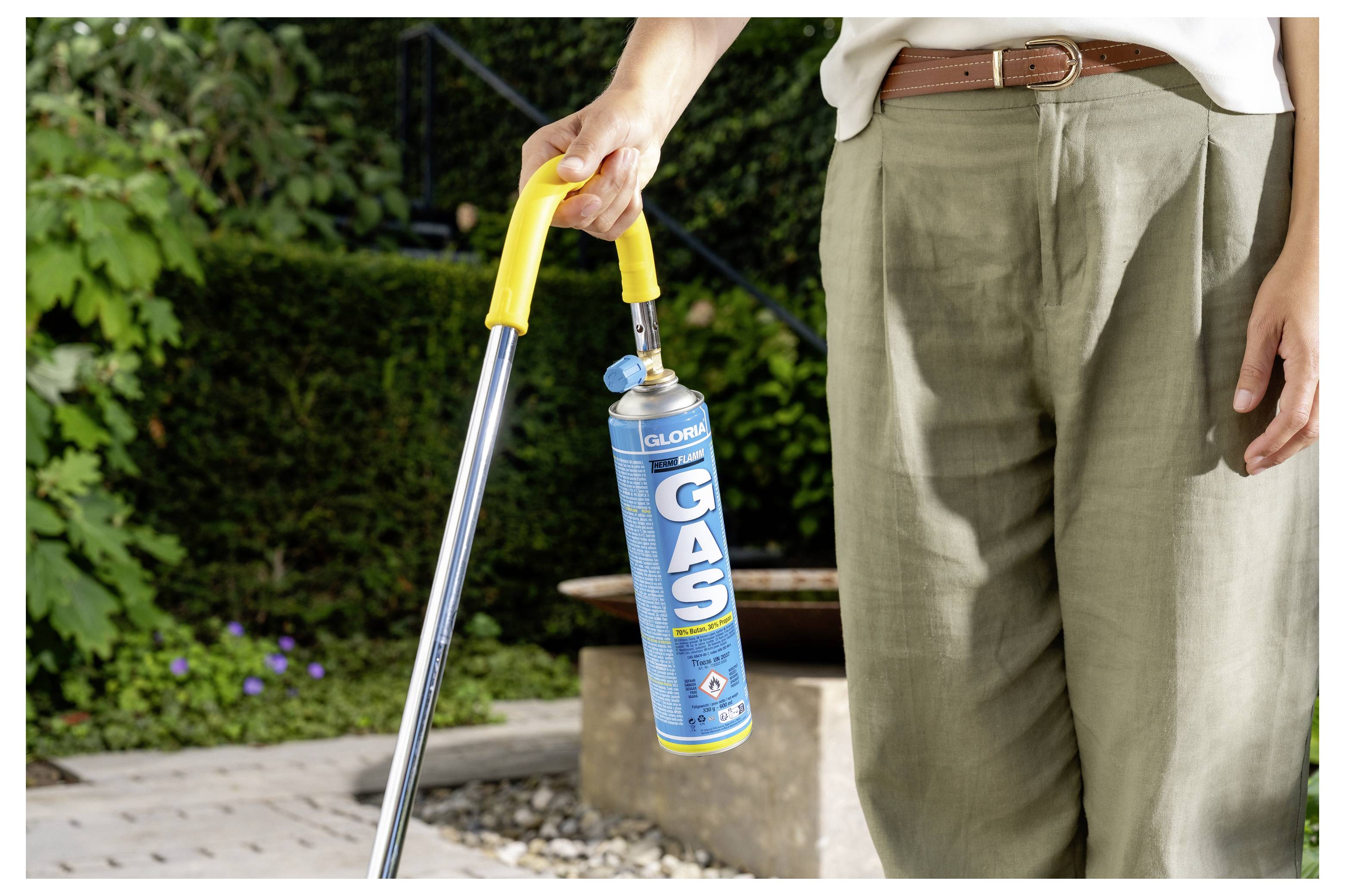 Person, die ein langes Feuerzeug hält und einen blauen Gaskartuschen im Freien in einem Garten- oder Terrassenbereich anzündet.