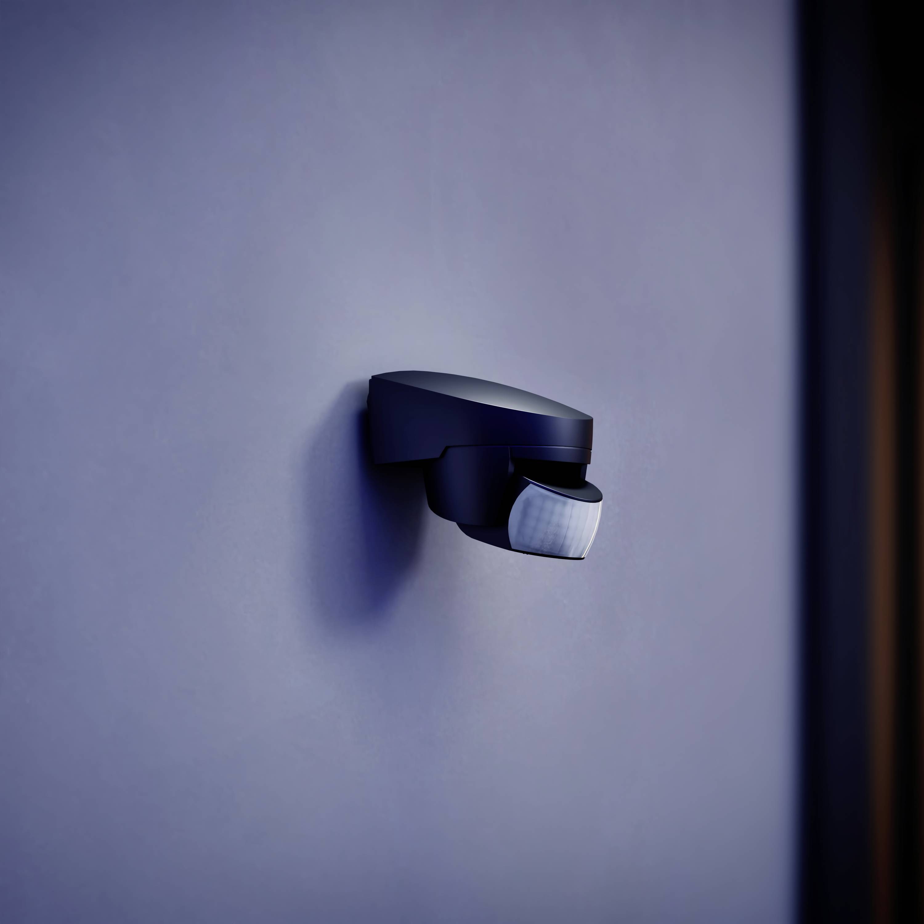 Wandmontierter Bewegungsmelder in modernem Design, an einer blauen Wand befestigt.