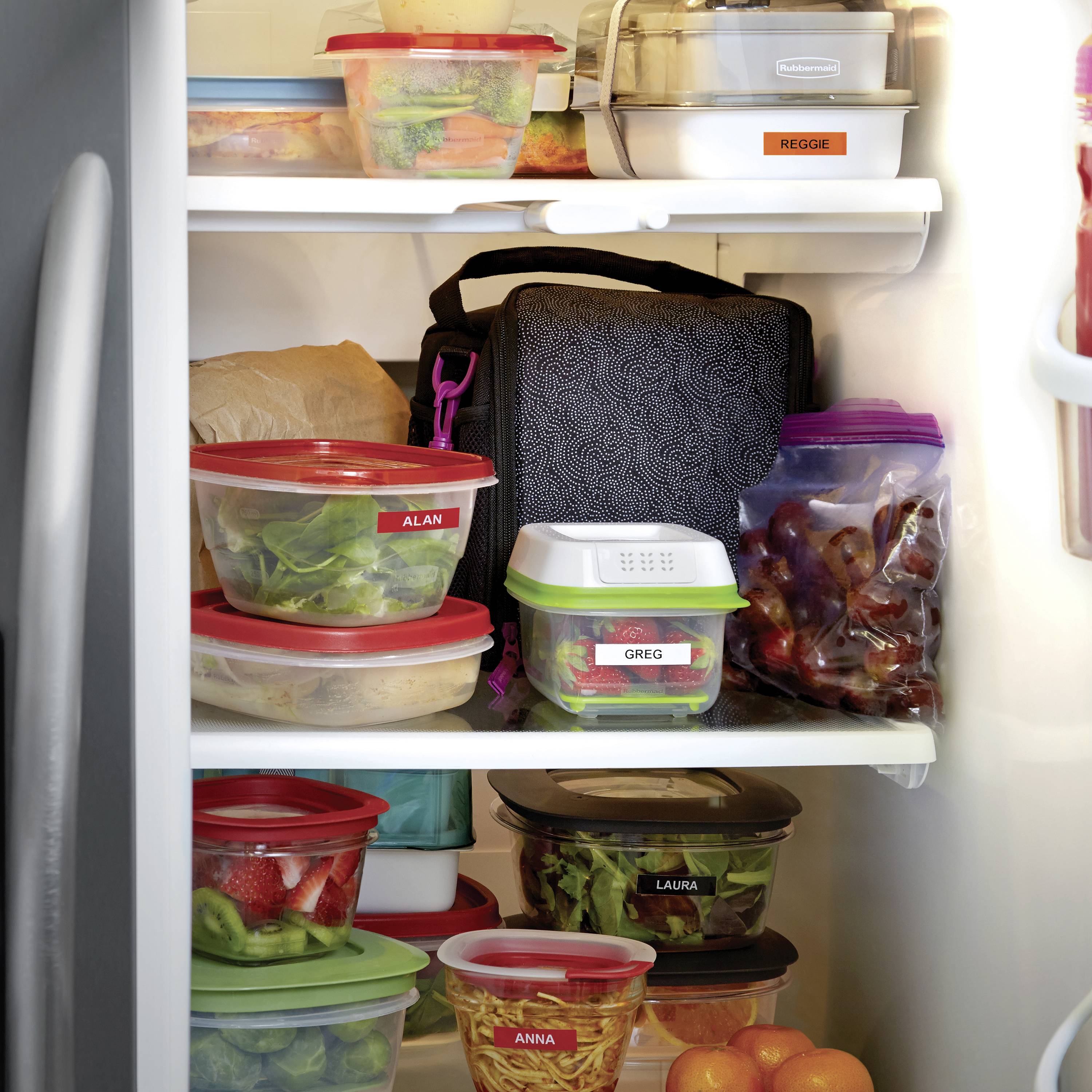 Ein geöffneter Kühlschrank zeigt mehrere beschriftete Plastikbehälter mit Lebensmitteln. Einige sind mit Namen markiert, wie 'Alan', 'Greg' und 'Laura'.