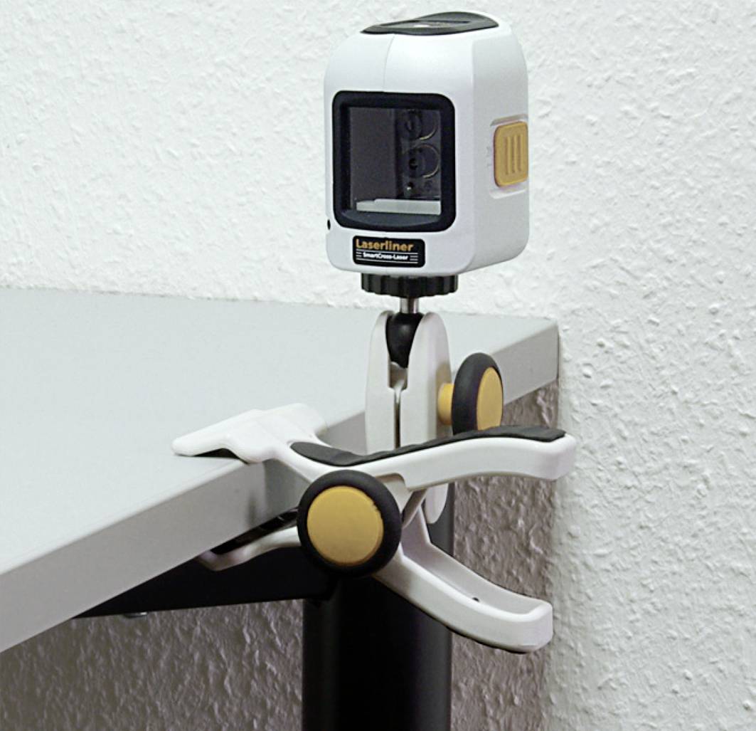 Eine Klemme befestigt einen Laser-Entfernungsmesser an einer Tischkante. Der Messgerät zeigt nach vorne und dient zur genauen Ausrichtung.