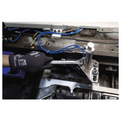 Die behandschuhte Hand einer Person bedient einen Schraubenschlüssel an einer Industriemaschine mit sichtbaren blauen Kabeln, was auf Wartungs- oder Reparaturarbeiten hindeutet.