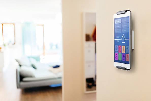 Ein Tablet an der Wand steuert Smart-Home-Funktionen in einem modernen Wohnzimmer. Im Hintergrund sind unscharfe Möbel erkennbar.