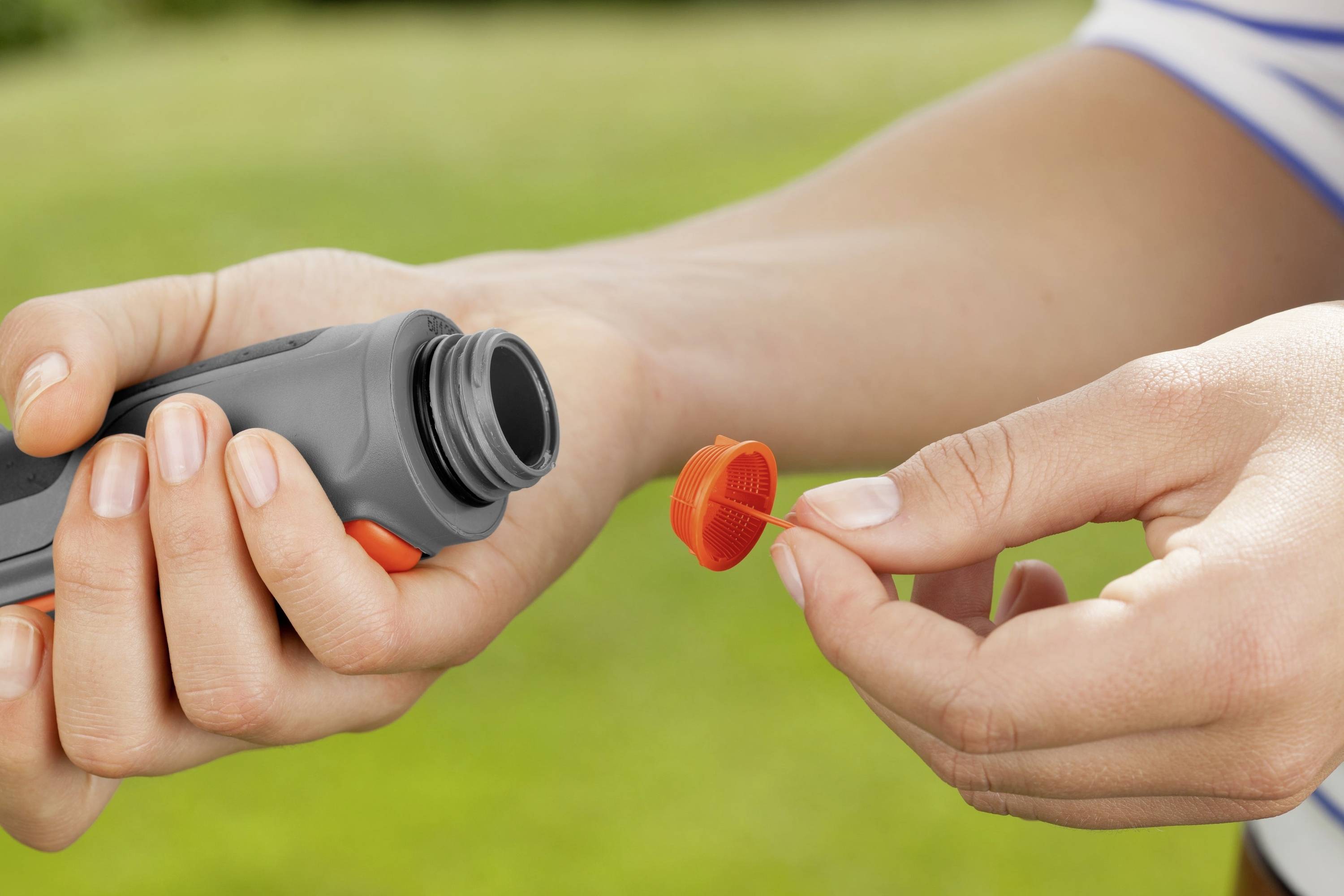 Person hält eine kleine geöffnete Plastikflasche in einer Hand und den roten Deckel in der anderen Hand, vor einem verschwommenen grünen Hintergrund.