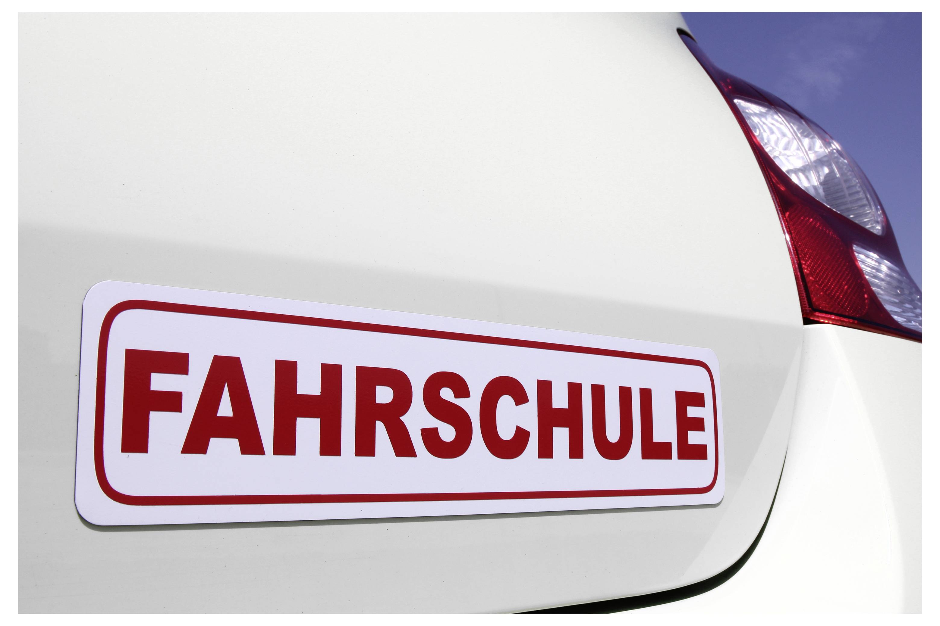 Nahaufnahme eines Autos mit einem roten „FAHRSCHULE"-Schild, das ein Fahrzeug einer Fahrschule anzeigt.