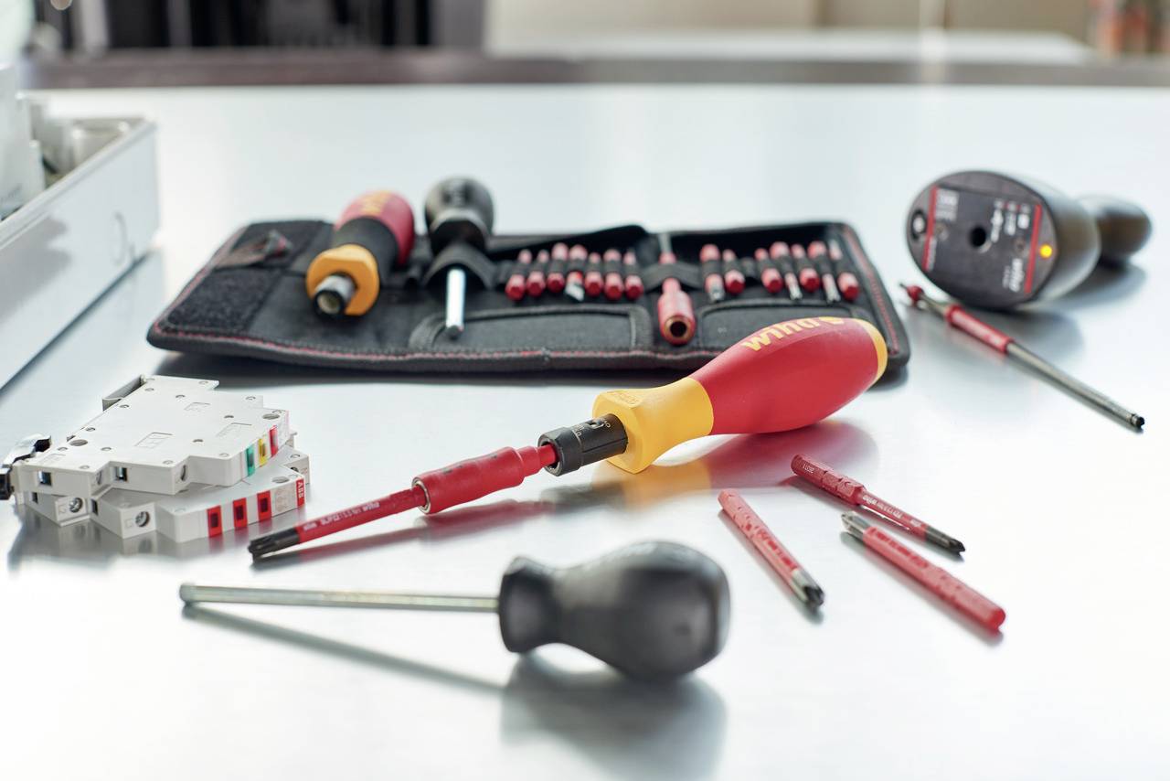 Verschiedene Schraubendreher und Bits auf einem Tisch neben einer Werkzeugtasche, bereit für eine Elektroinstallation oder Reparatur.