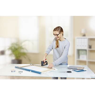 Frau mit Brille befestigt Stoff auf einem Holzrahmen mit einem Tacker in einem hellen Büro mit Tisch.