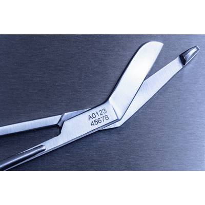 Metallische medizinische Schere mit Nummer 'A0123 45678' auf der Klinge, auf einer glatten, grauen Oberfläche liegend.