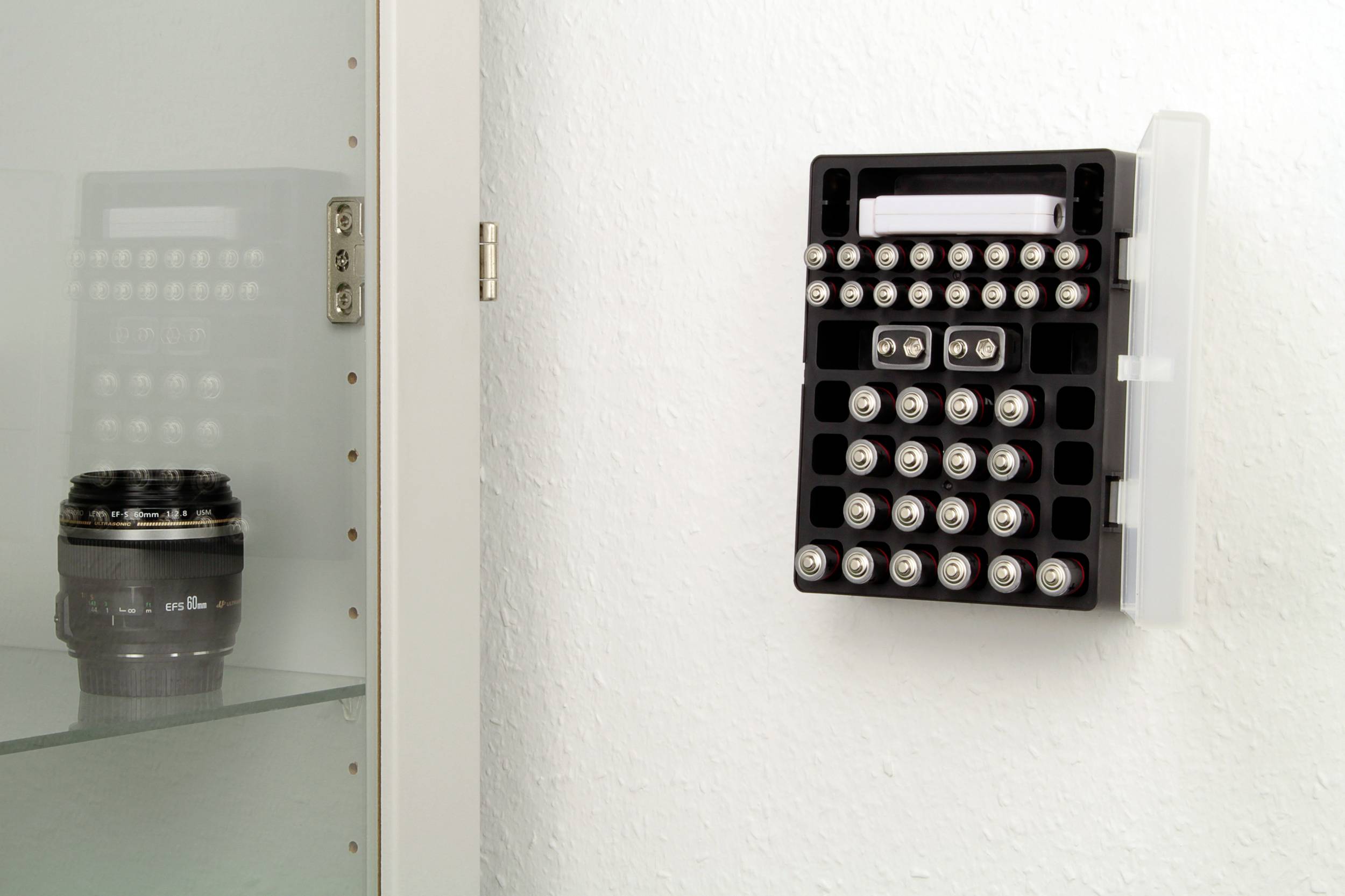 Eine Wandhalterung mit mehreren AA- und AAA-Batterien, daneben ein Regal mit einer Kameralinse.