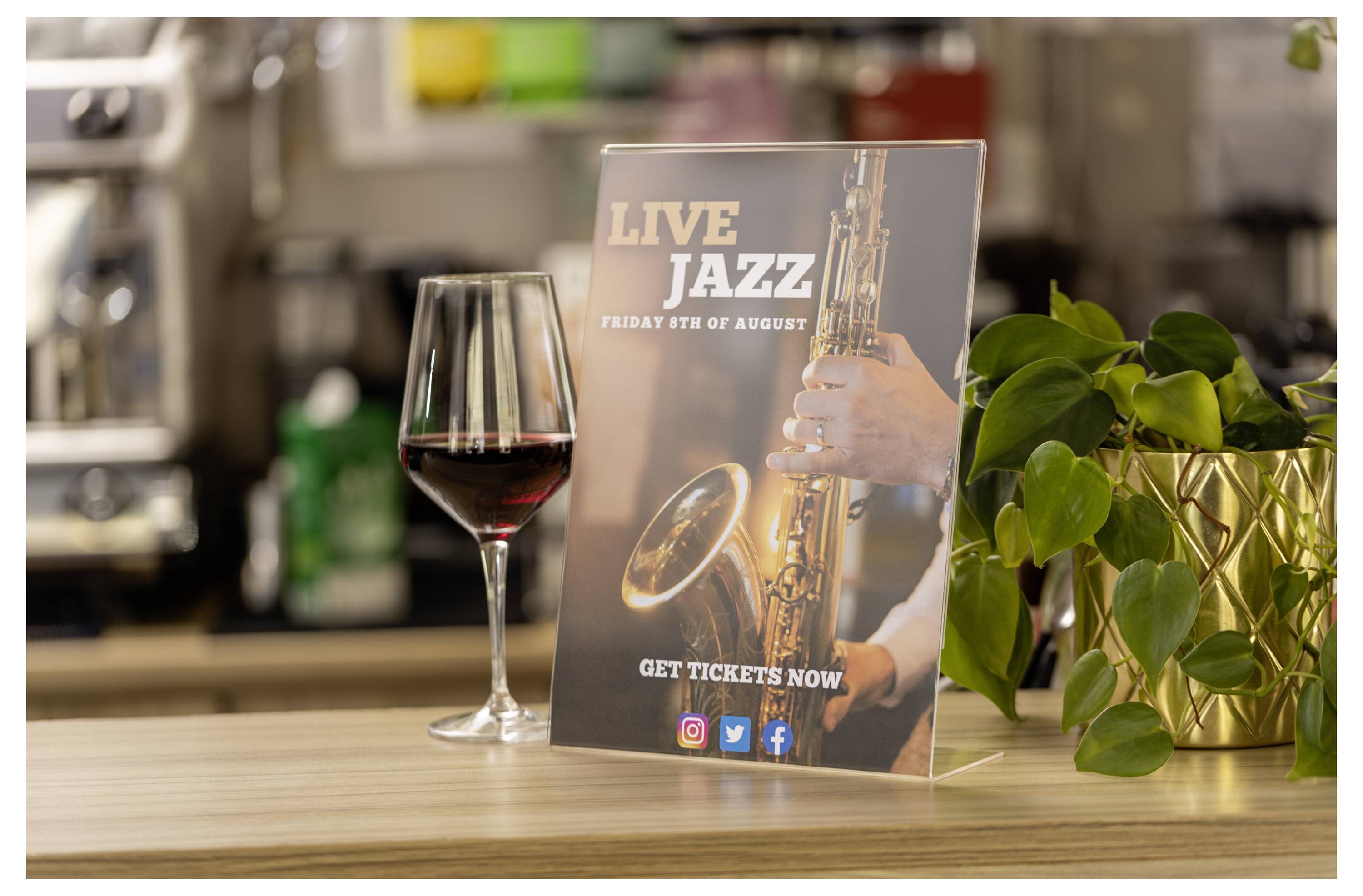 Ein „Live Jazz"-Veranstaltungsflyer auf einem Tresen neben einem Glas Rotwein und einer Topfpflanze, der für Freitag, den 6. August wirbt und „Jetzt Tickets kaufen".