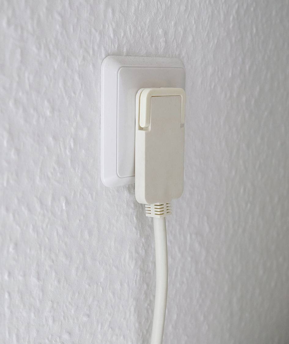 Ein weißes LAN-Kabel ist in eine Wandsteckdose eingesteckt, vor einer strukturierten weißen Wand.