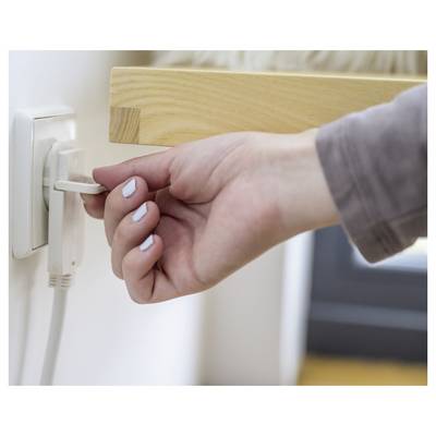Hand steckt ein weißes Gerät in eine Wandsteckdose neben einem Holztisch.