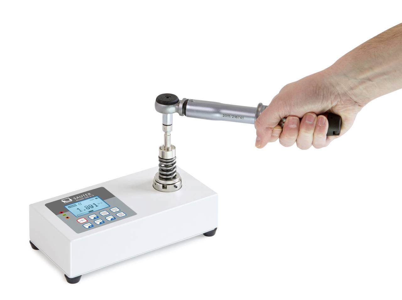 Eine Hand hält einen Drehmomentschlüssel, der auf einem weißen Gerät mit digitalem Display befestigt ist.