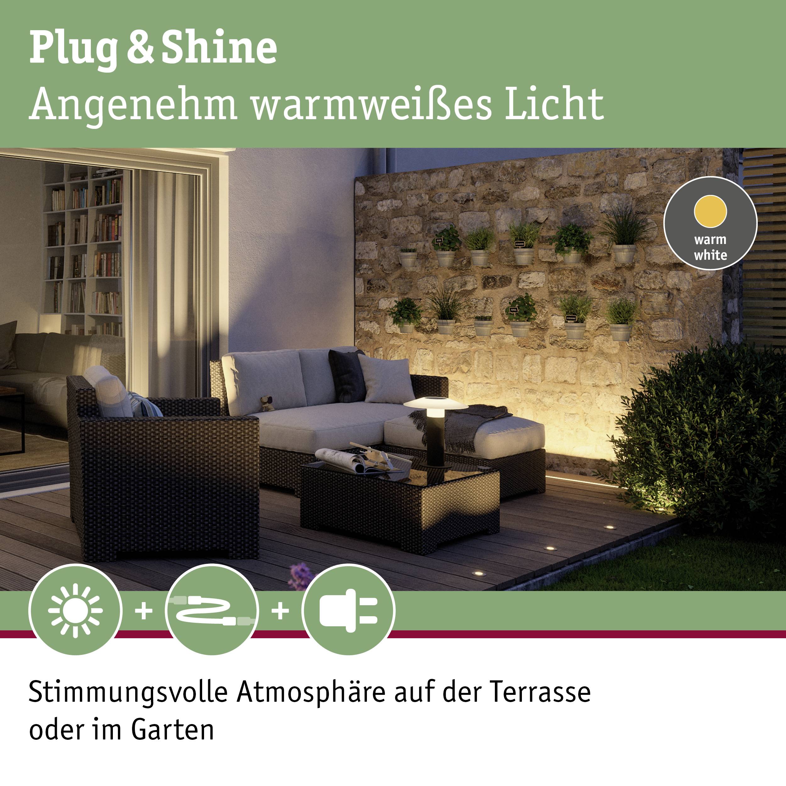 'Sofa mit Kissen auf beleuchteter Terrasse bei Nacht, umgeben von Pflanzen an einer Steinmauer. Text: Stimmungsvoll im Garten.'