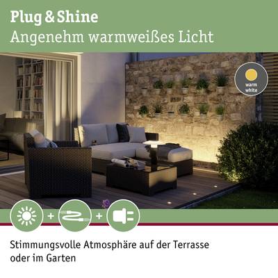 'Sofa mit Kissen auf beleuchteter Terrasse bei Nacht, umgeben von Pflanzen an einer Steinmauer. Text: Stimmungsvoll im Garten.'