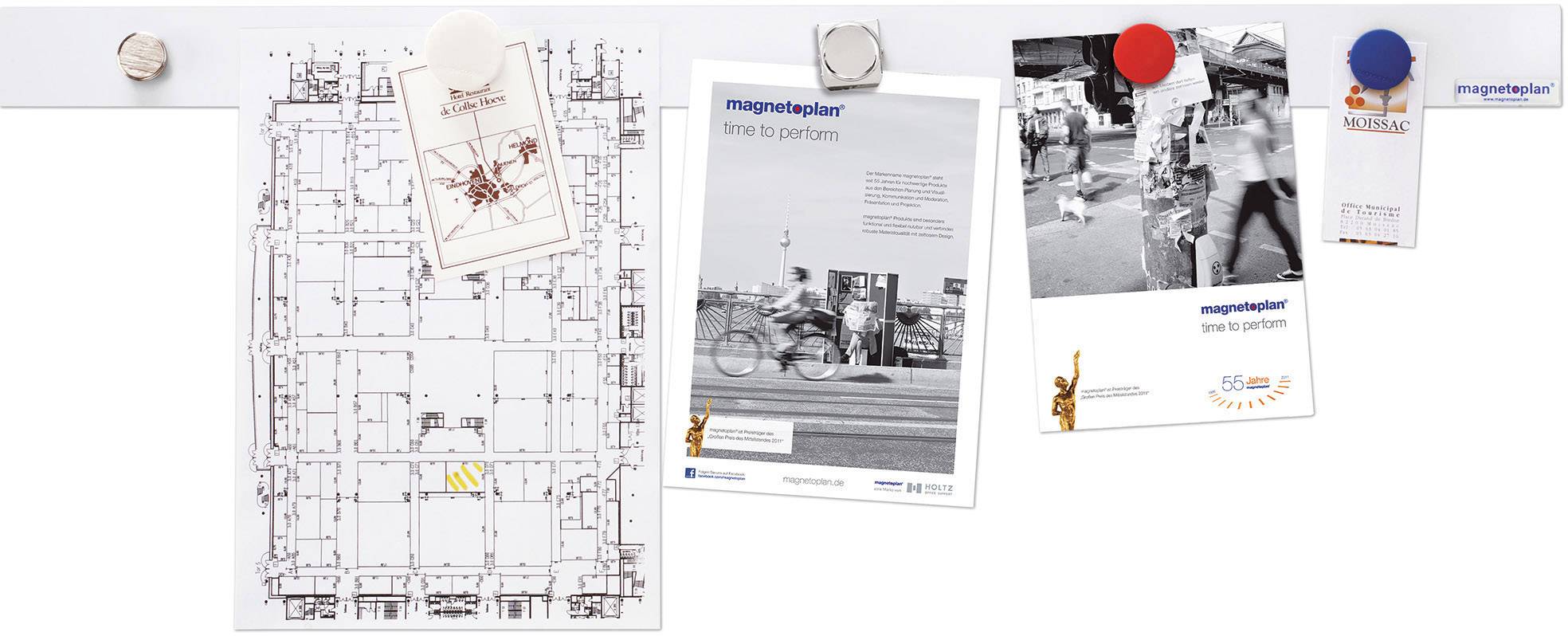 'Ein Architekturplan an einer Pinnwand, daneben drei Fotos und ein Kalenderblatt befestigt mit bunten Magneten.'