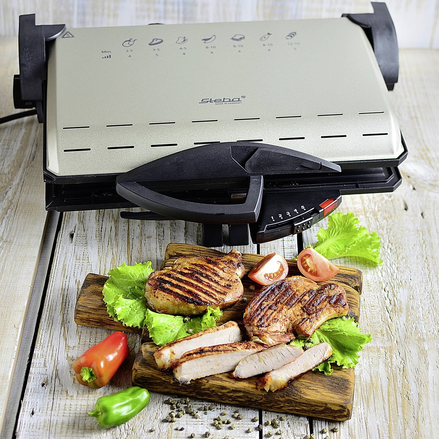 Ein Kontaktgrill auf einem Tisch, Grillplatten offen, darauf gegrilltes Fleisch und Gemüse.