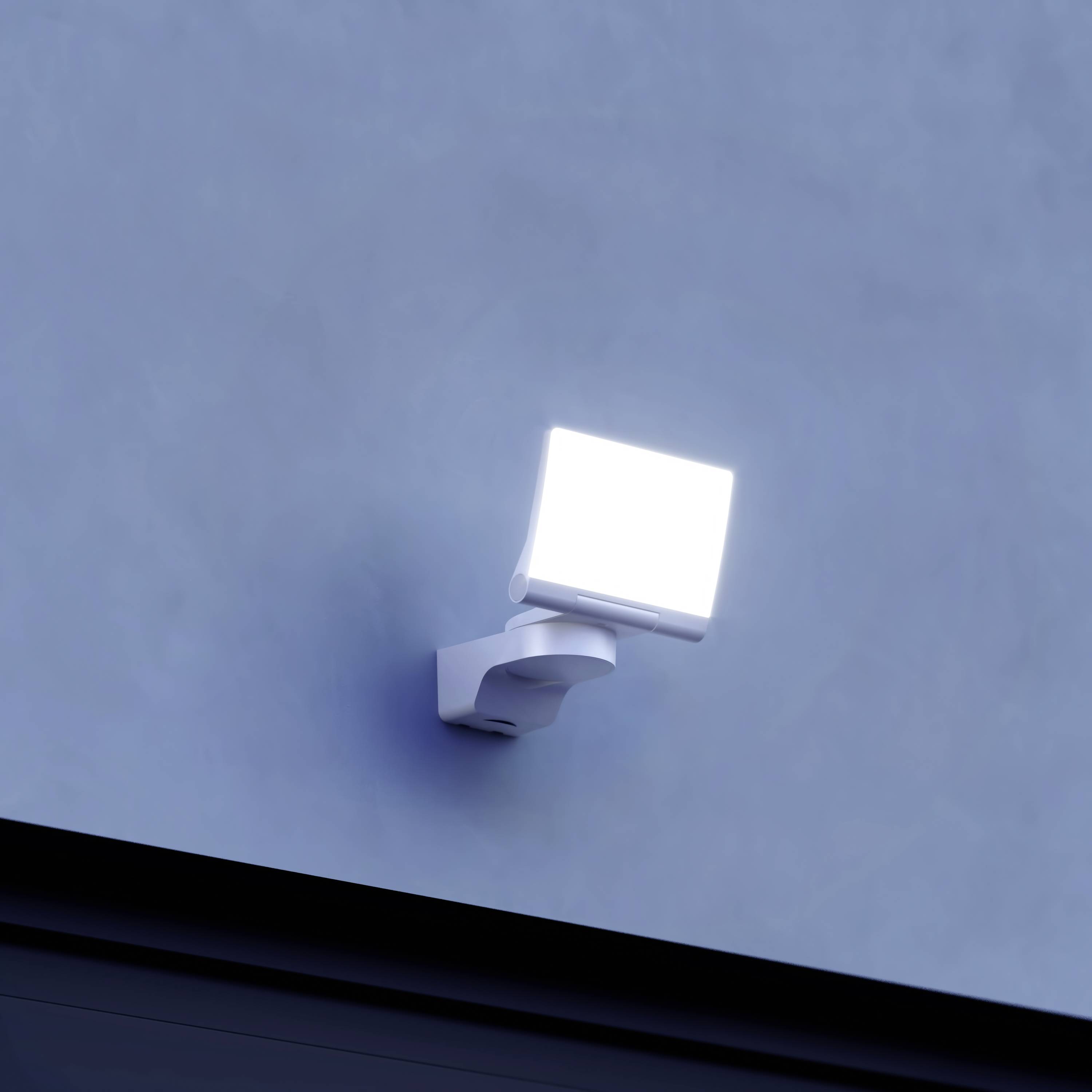 Eine helle Sicherheitslampe an einer grauen Wand leuchtet in der Dämmerung, sorgt für Außenbeleuchtung und erweitert das Sichtfeld.